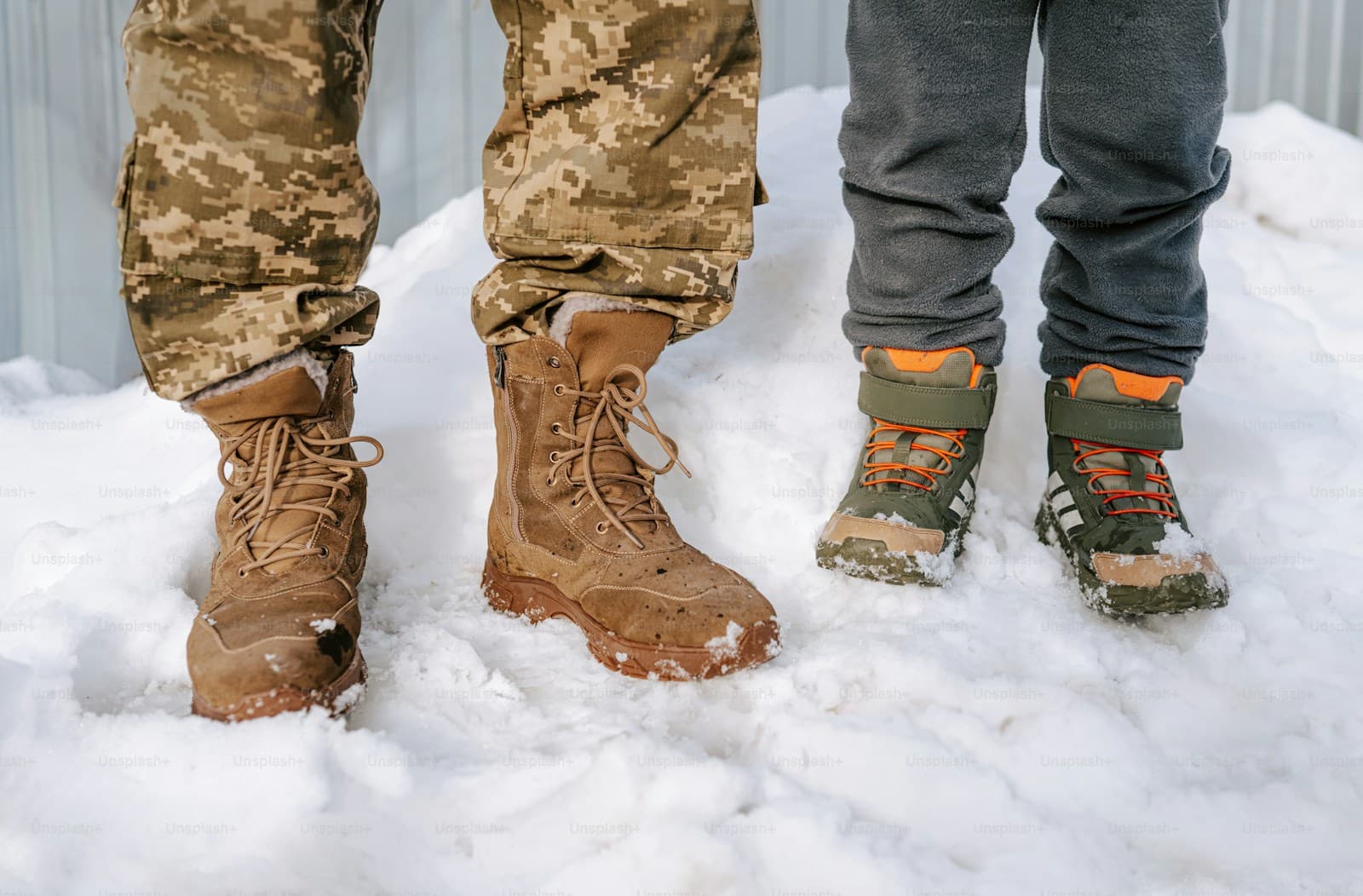 Legs of two people in deep snow, one in desert camouflage and tan combat boots