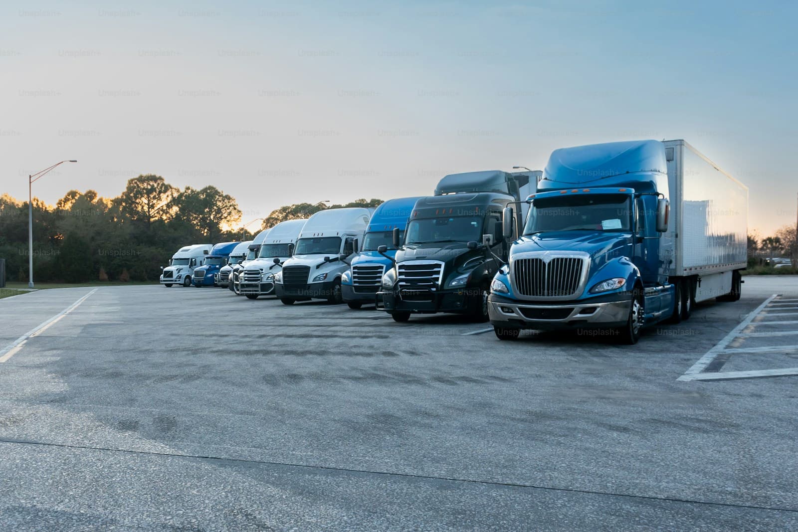 Semi-trucks parked in diagonal spaces across a large lot at first light