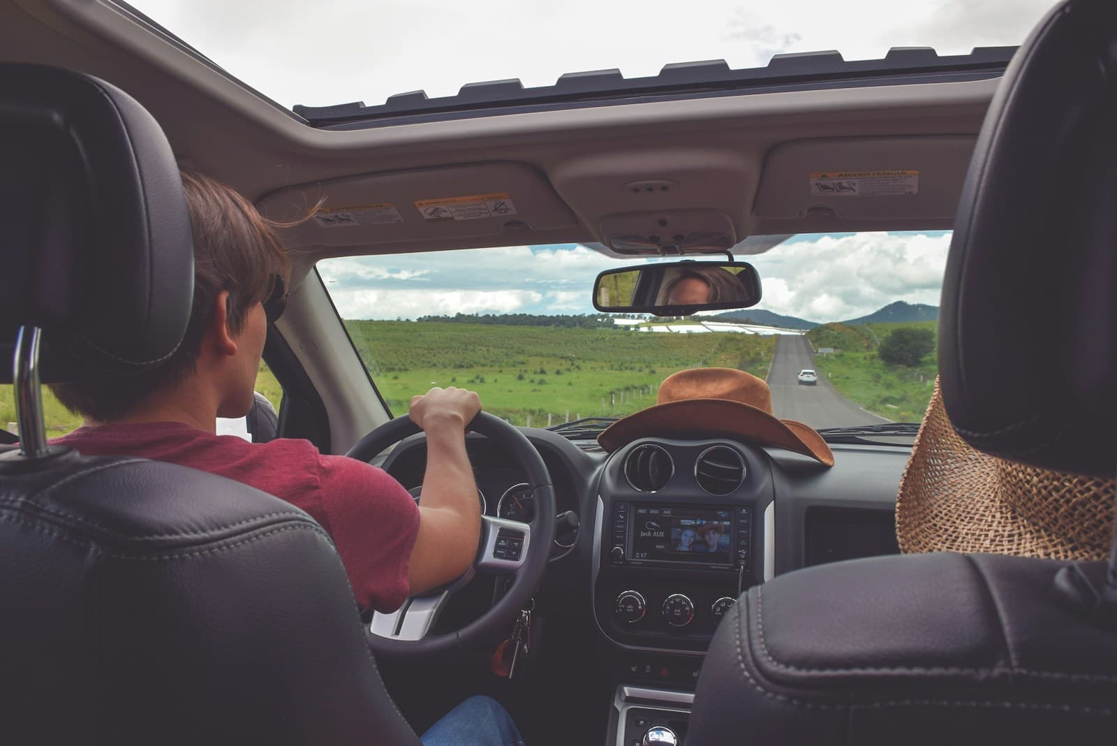 Driver in a red shirt and a hat-wearing passenger traveling a rural road