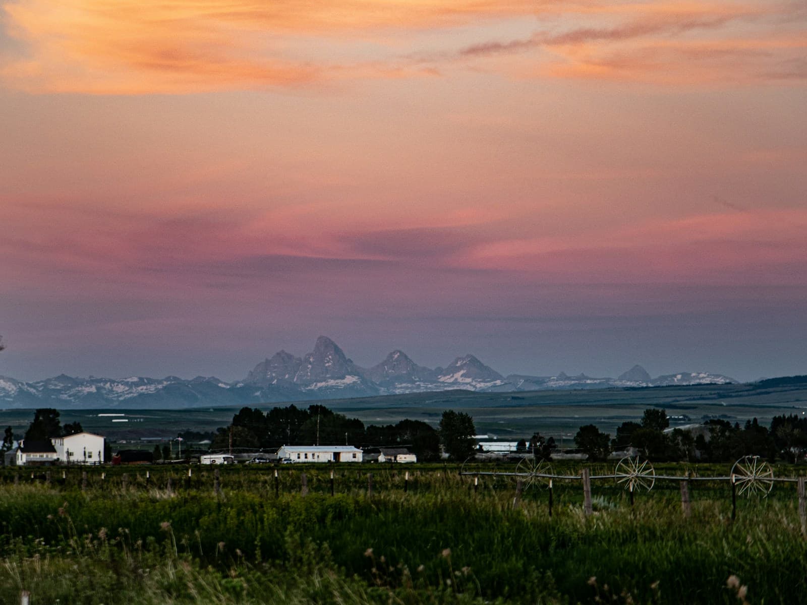 Rural farmland with white buildings and mountains in background during colorful sunset with pink and orange sky