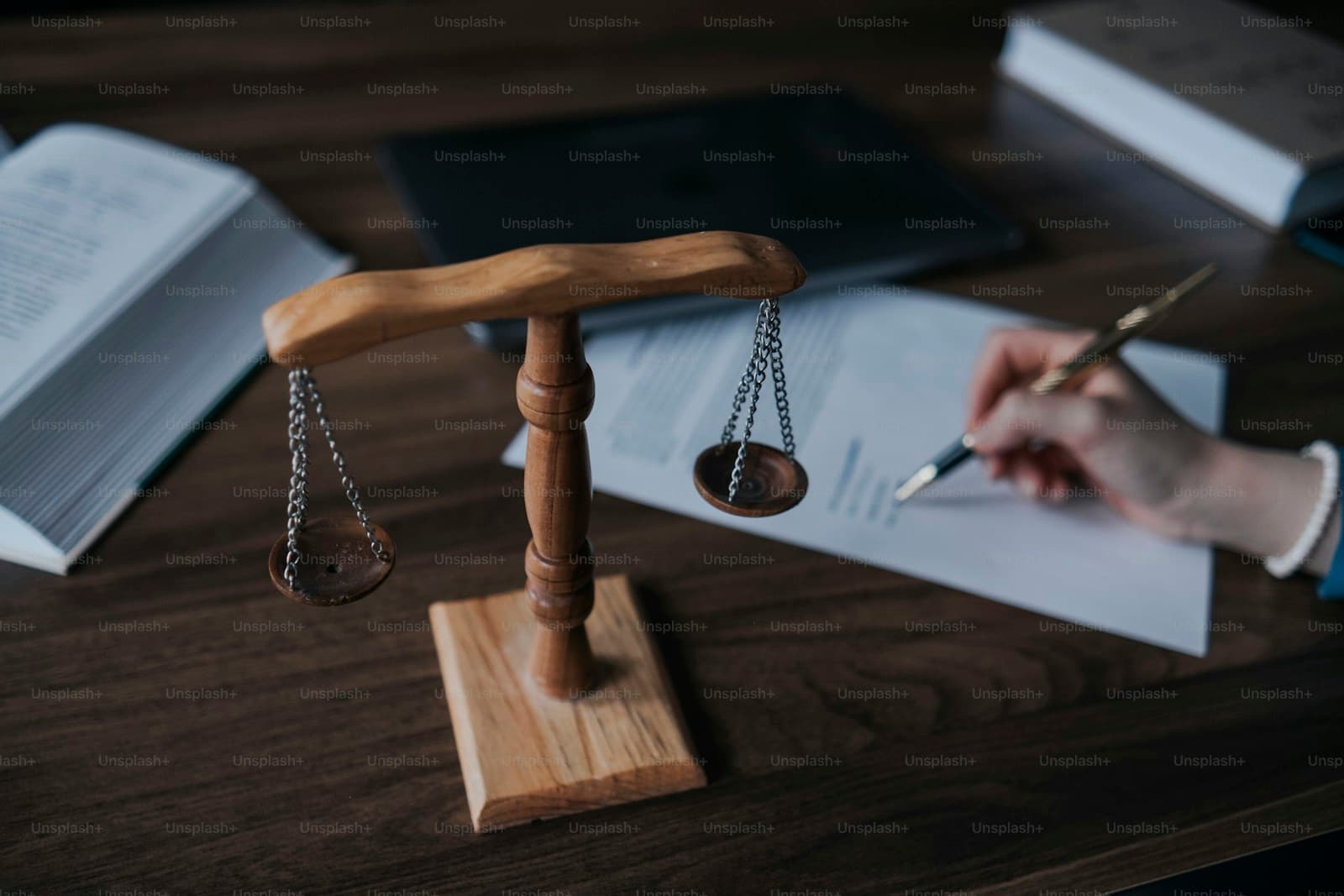 Wooden scales of justice on desk with legal documents, books, and hand writing with pen