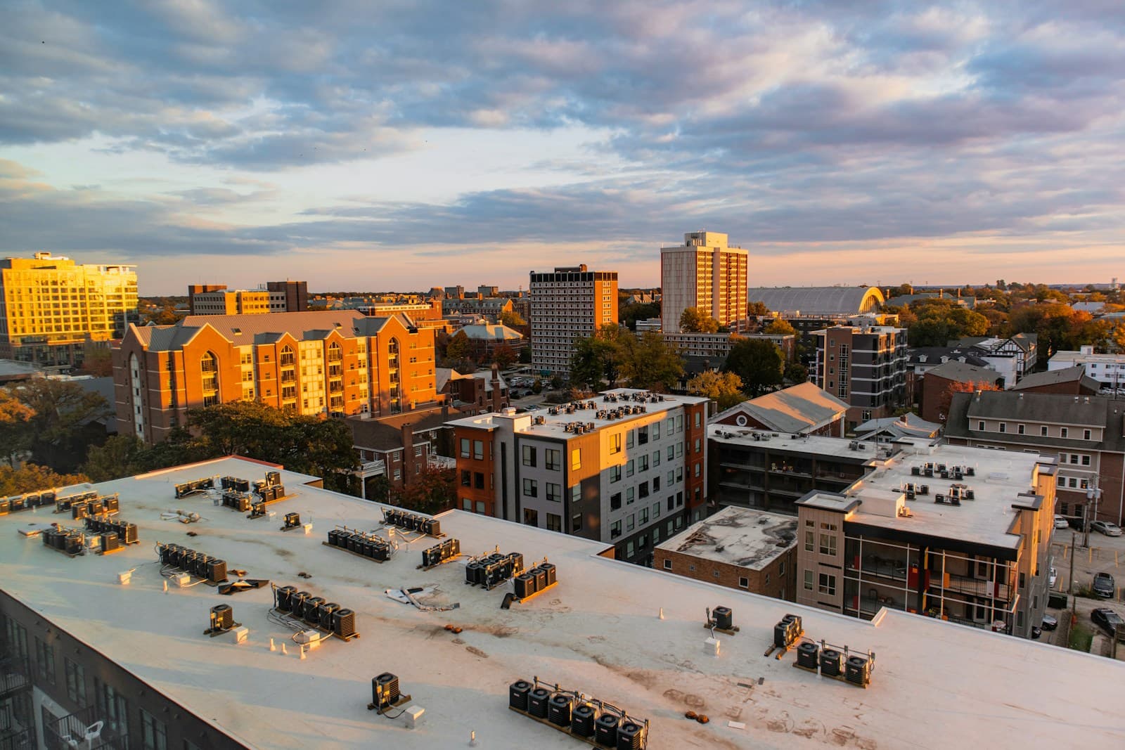 Aerial view of city buildings at sunset with rooftop HVAC equipment in foreground and cloudy sky