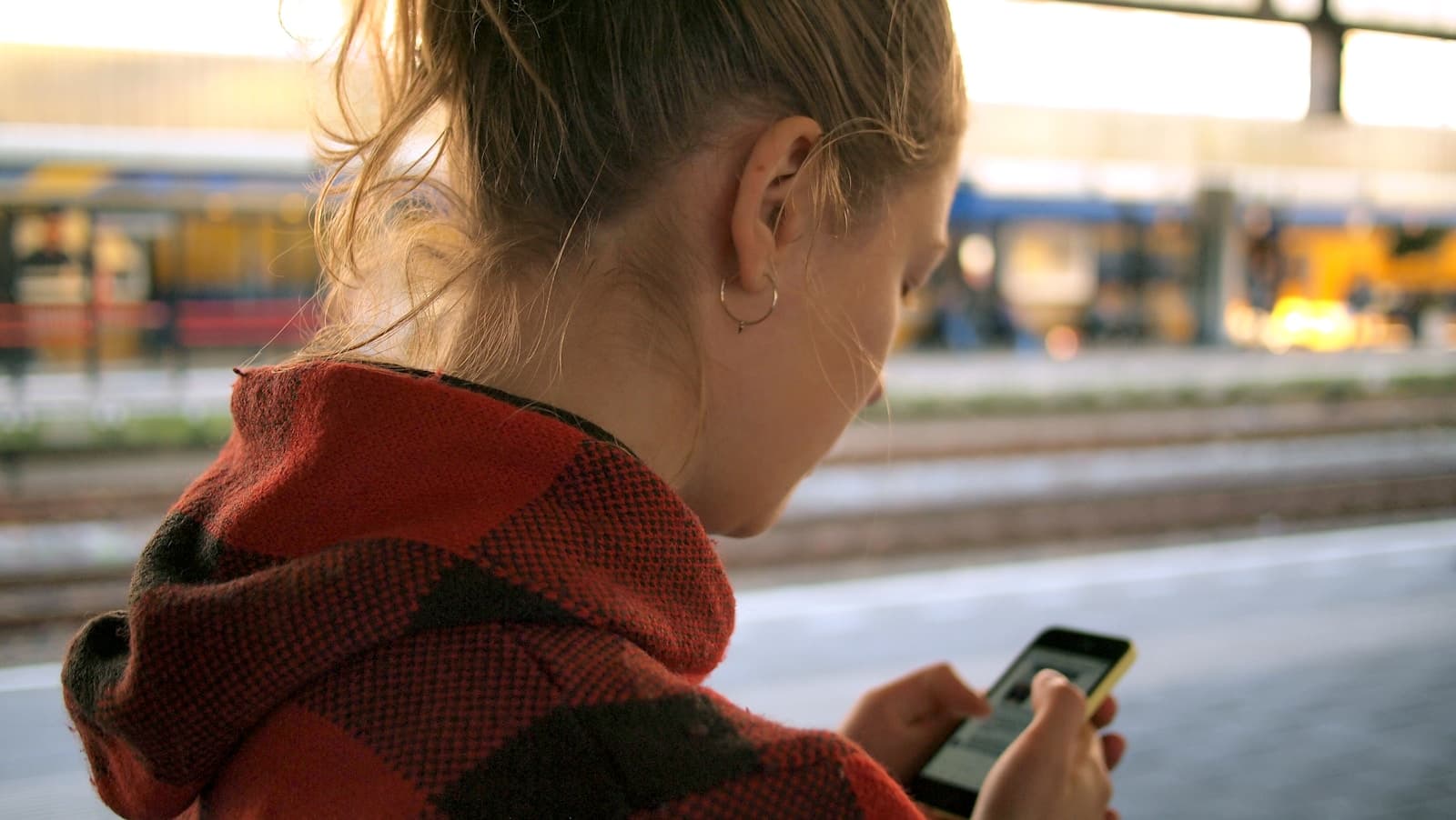 Young woman in a patterned hoodie checking her phone on a transit platform