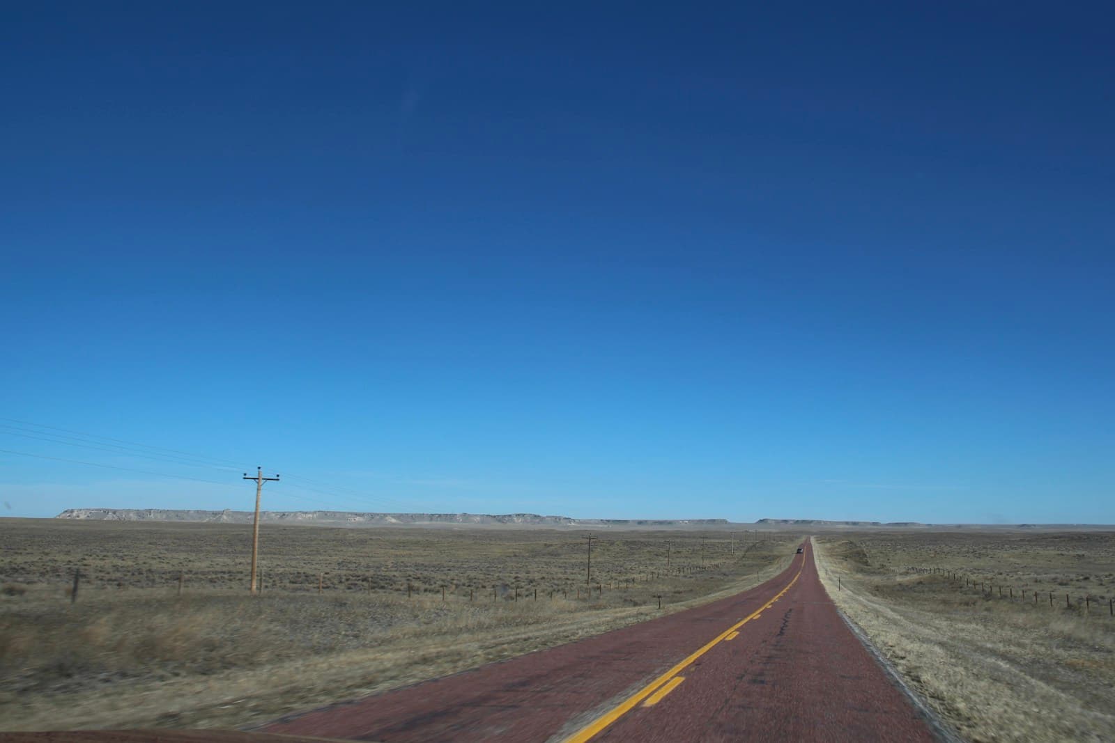 Empty desert highway stretching to horizon under clear blue sky with power lines and barren landscape