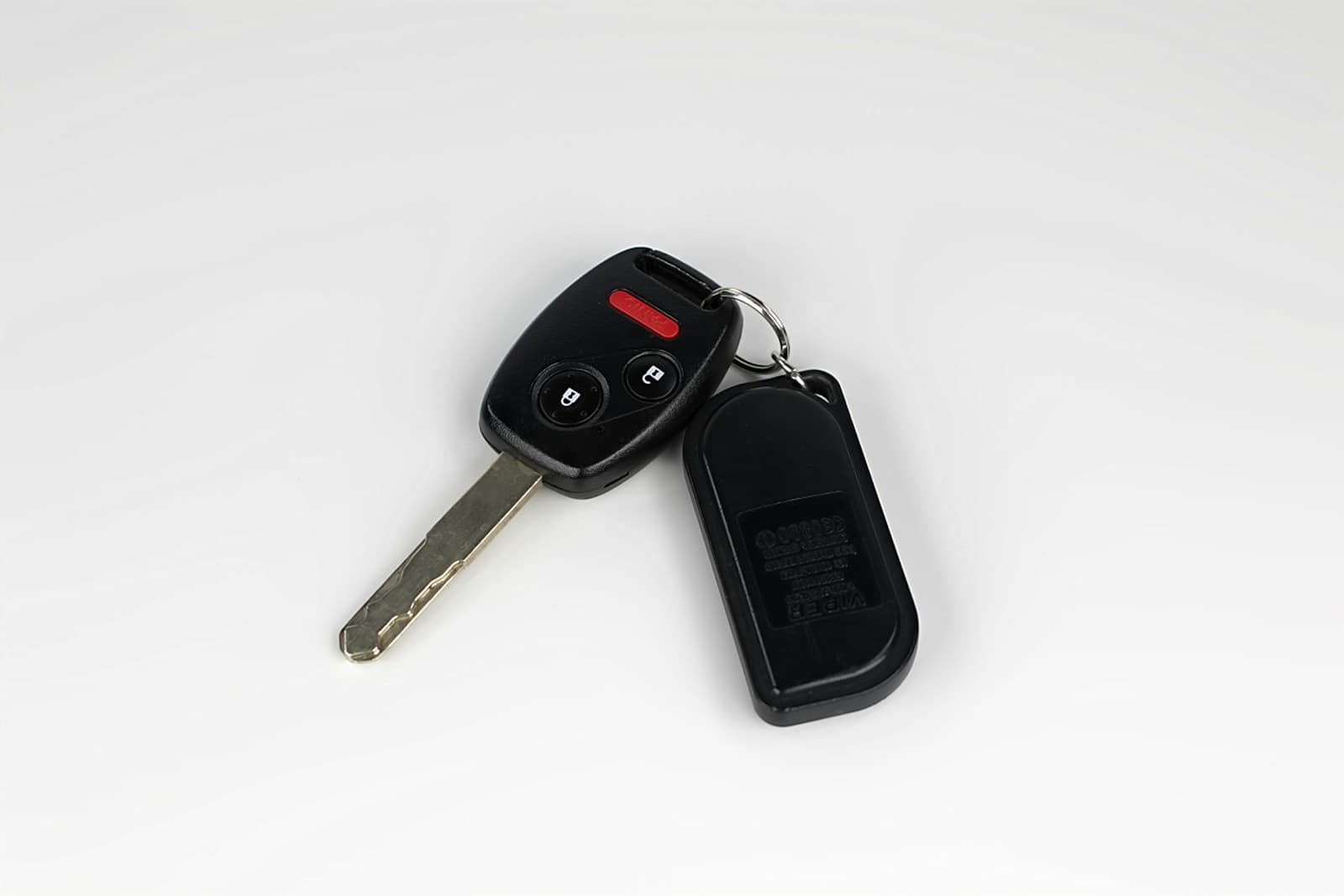 Black car key fob with remote buttons and metal key blade next to black remote device on white background