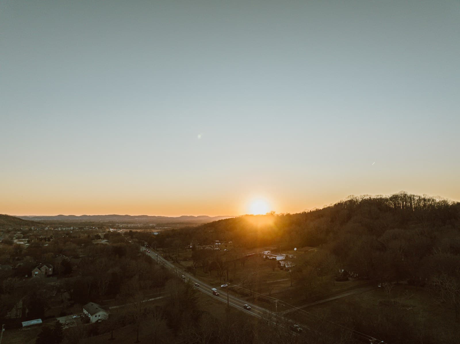 Aerial view of sunset over rural valley with hills, houses, and winding roads in golden light