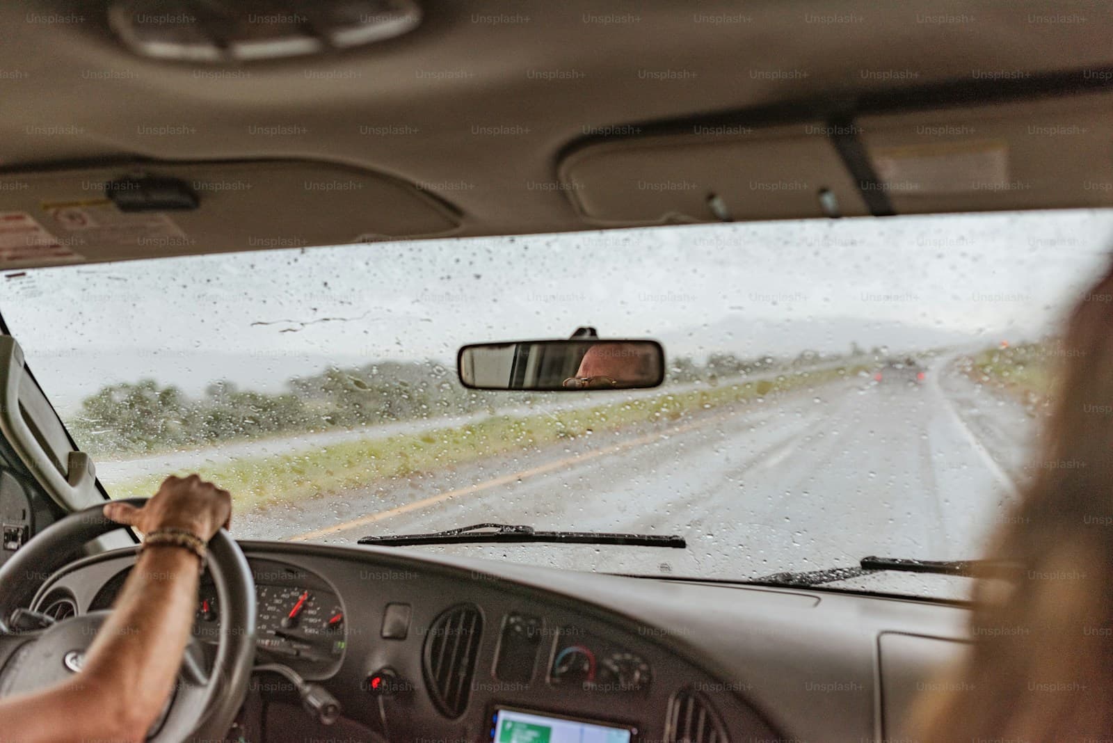 Driver on a wet rural road in the rain with raindrops beading on the windshield