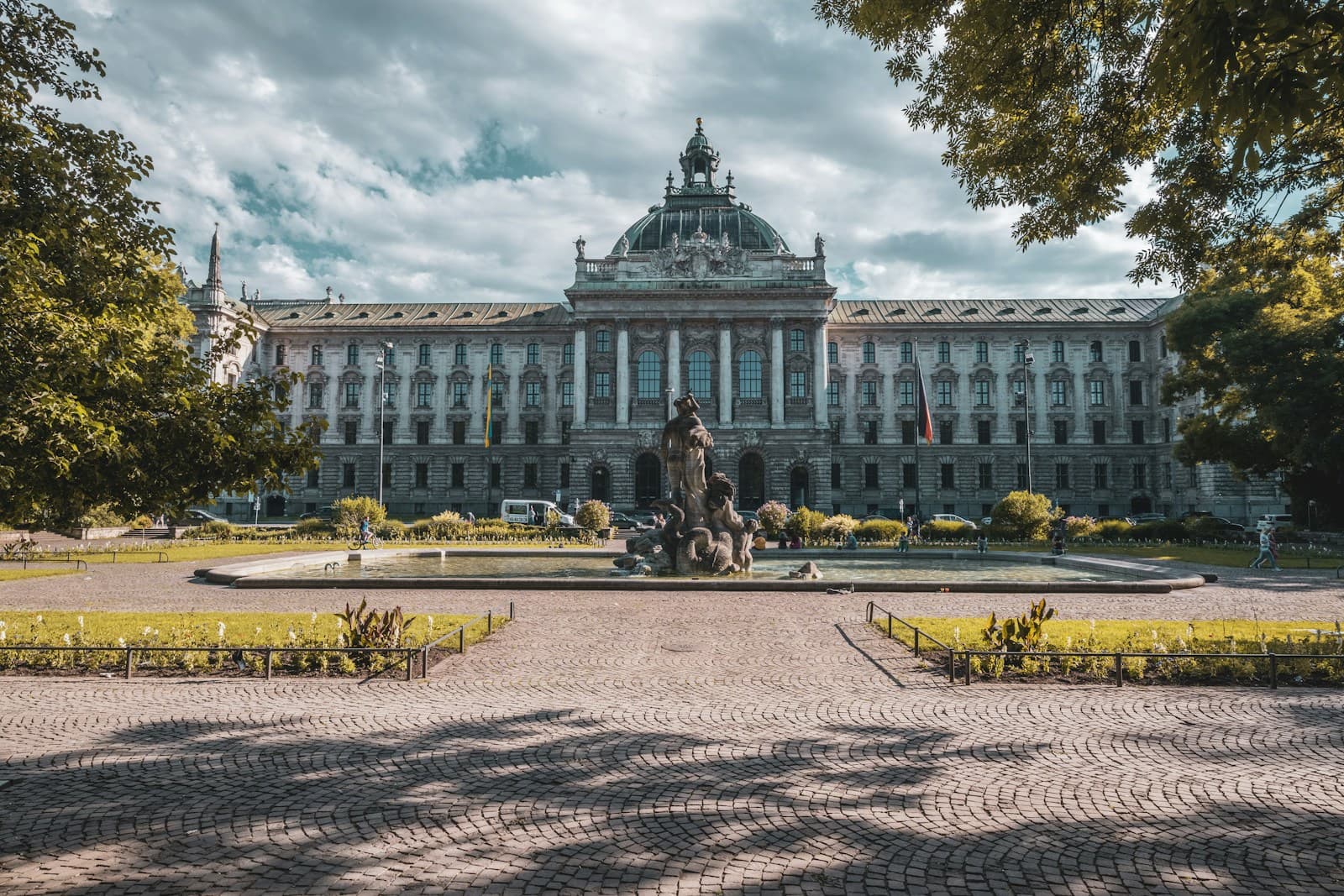 Neoclassical government building with dome and columns behind formal plaza with monument and gardens