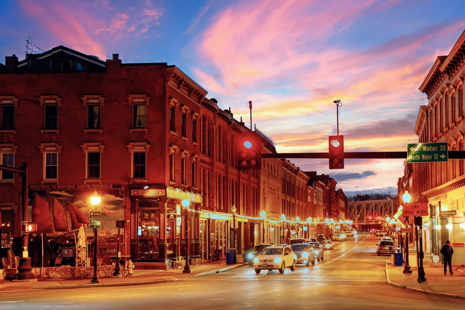 Historic downtown street at sunset with red brick buildings, colorful sky, and warm street lighting