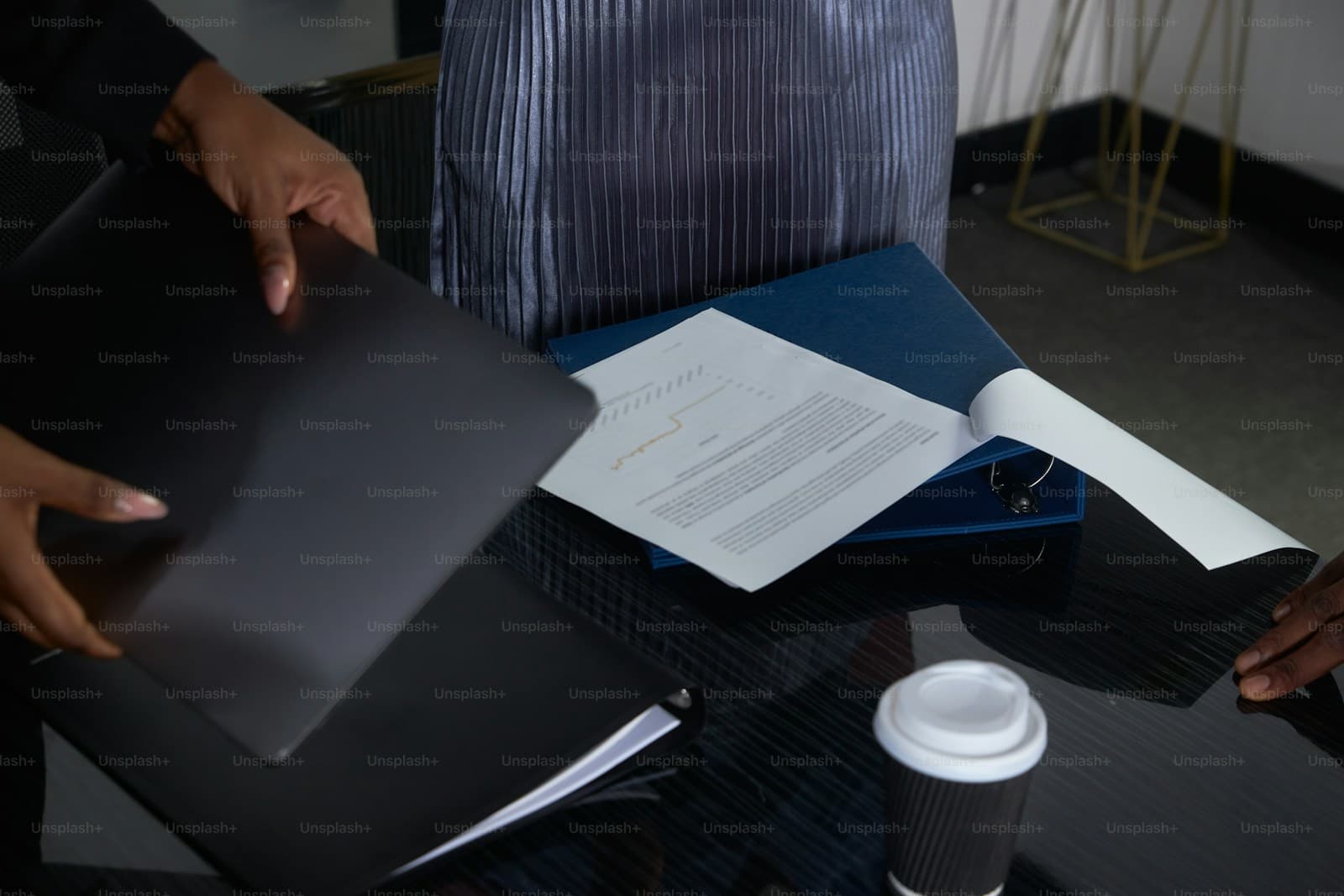 Person in a striped shirt reviewing papers at a desk with a laptop and coffee