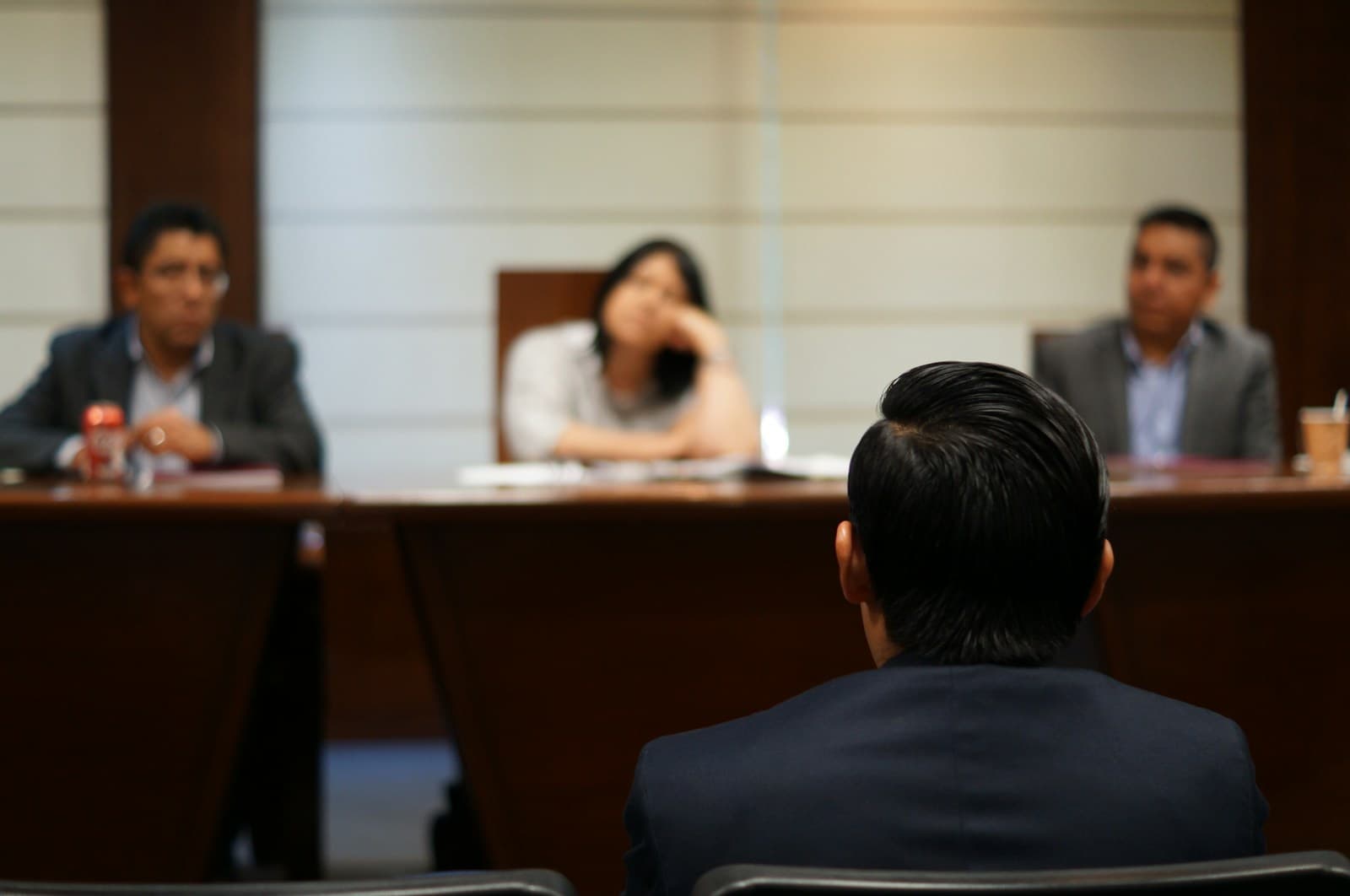 Person in suit facing three people seated at conference table in formal meeting room