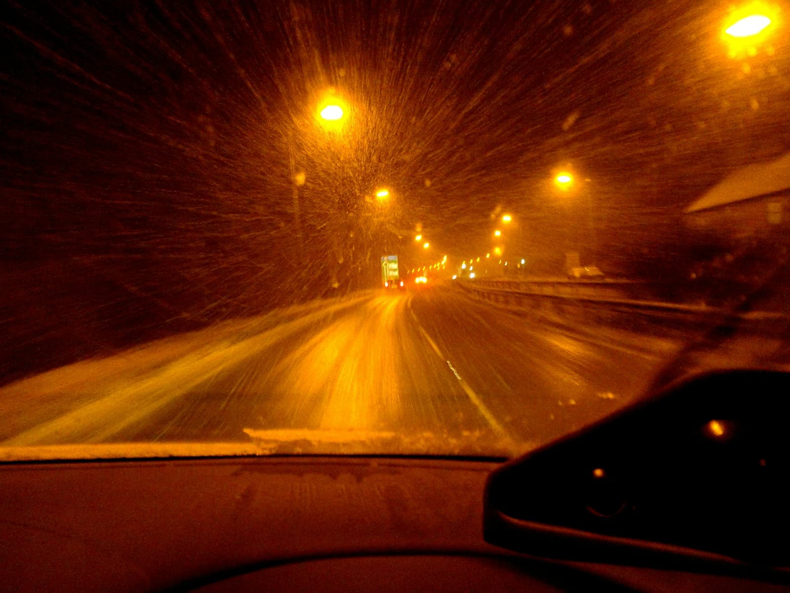 Driving a snowy road at night with streetlights flaring through the falling snow