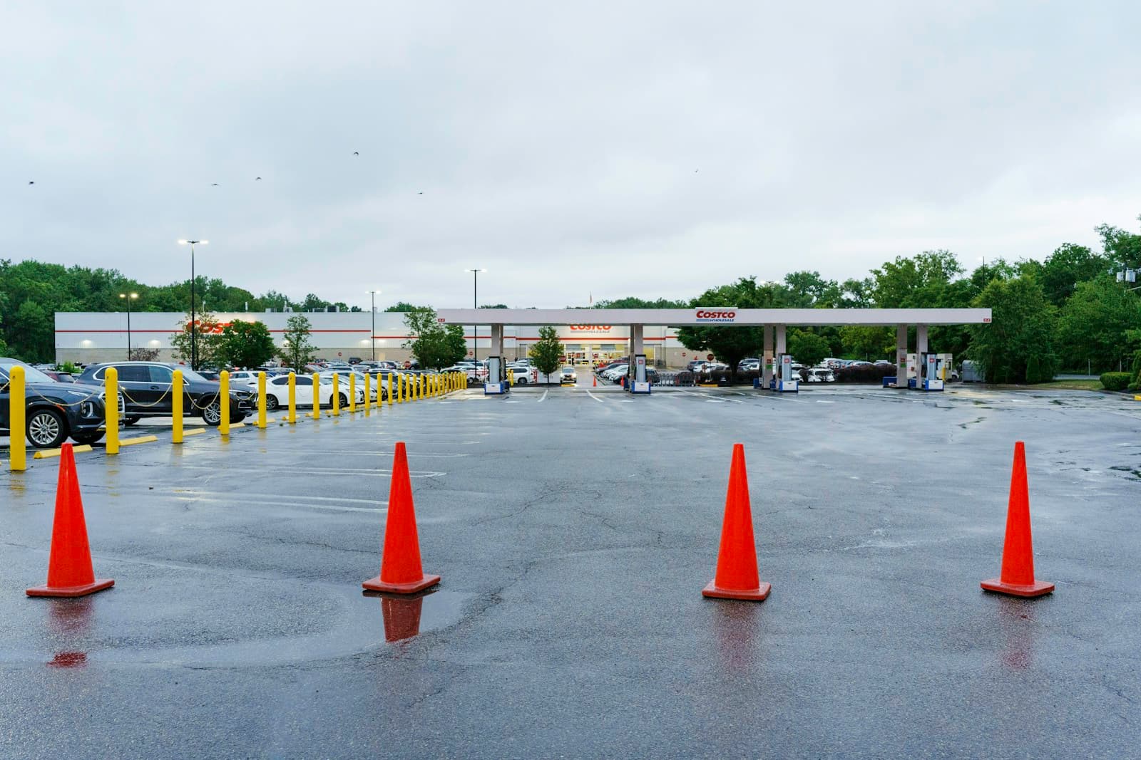 Four orange traffic cones on wet asphalt in front of a gas station with overcast sky