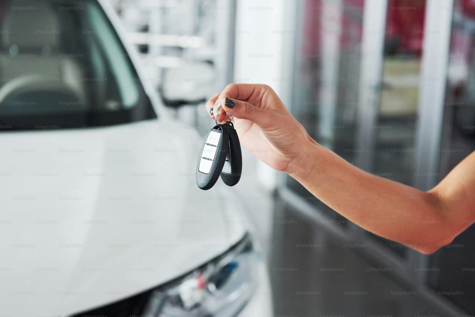 Hand holding car keys in front of white car at dealership