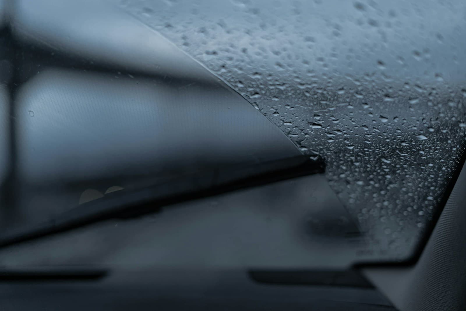 Rain-covered windshield seen from inside a car with the wipers mid-sweep