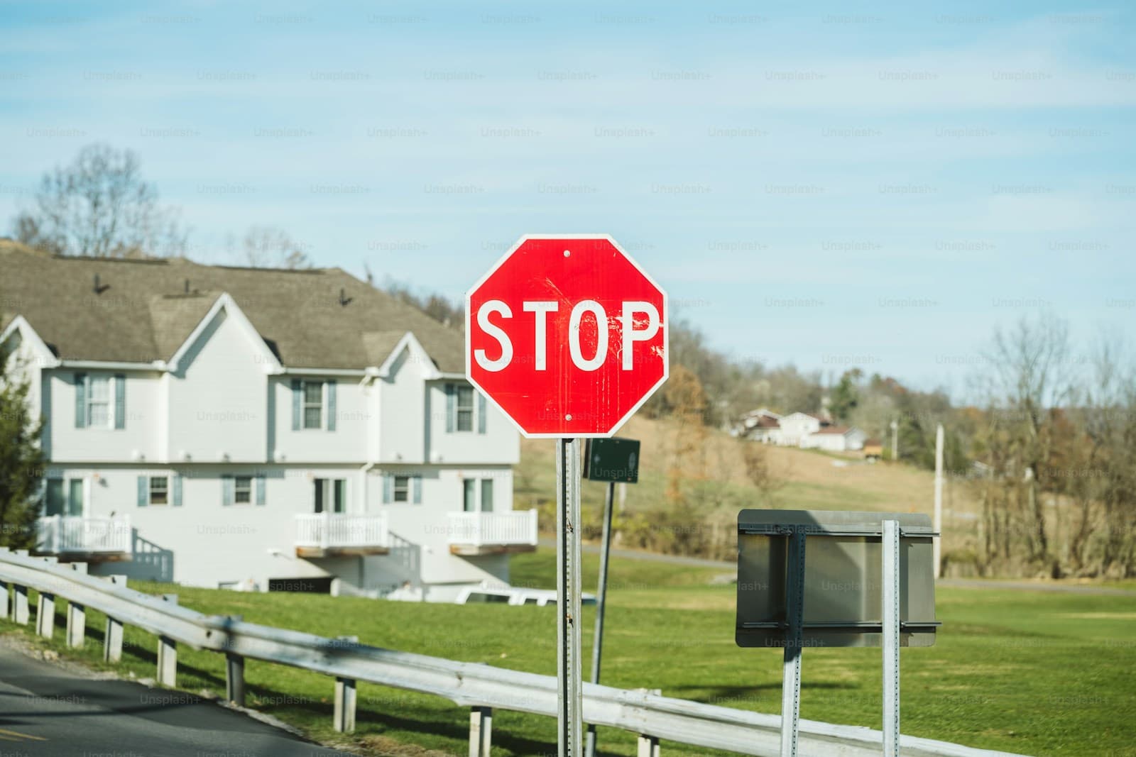 Red stop sign on residential street with white townhouses and green hills in background
