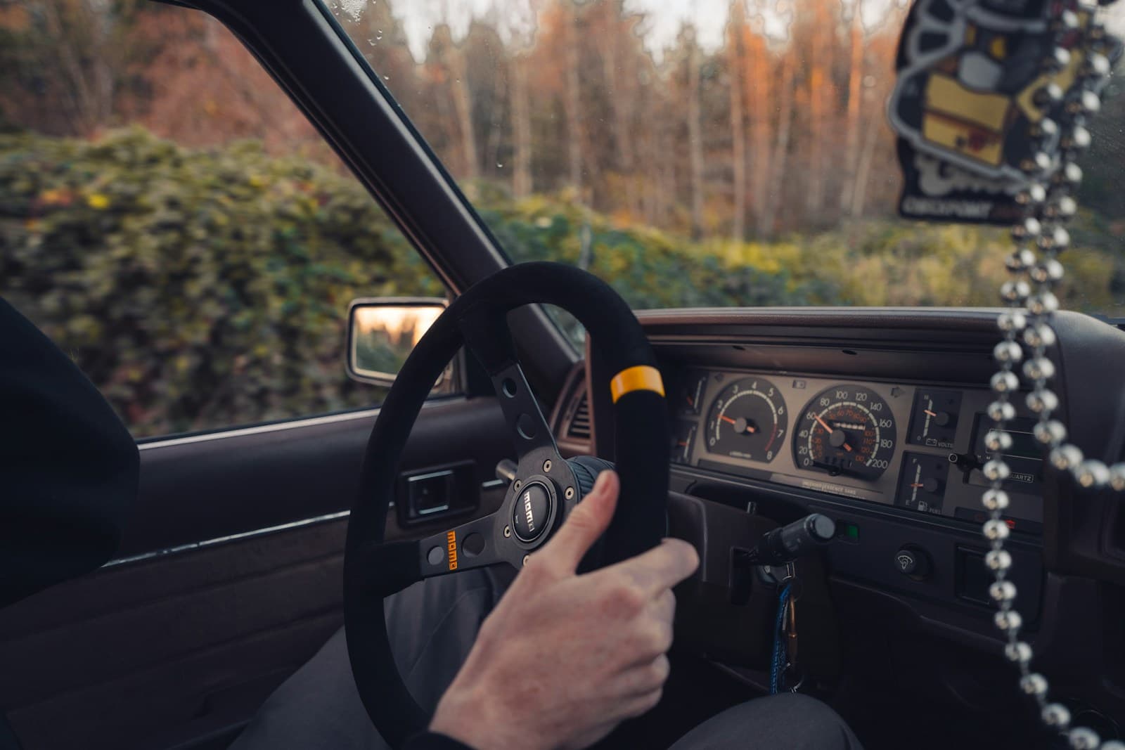 Driver at the wheel of a vintage car with analog gauges on an autumn wooded road