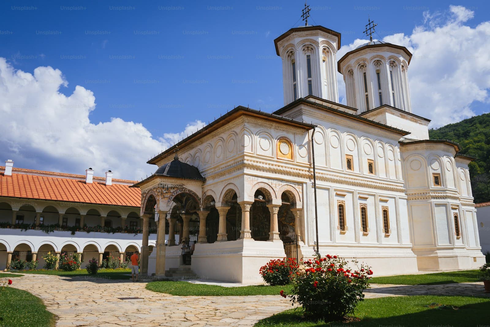 Orthodox monastery with white stone walls, twin bell towers, arched colonnade and red tile roof under blue sky