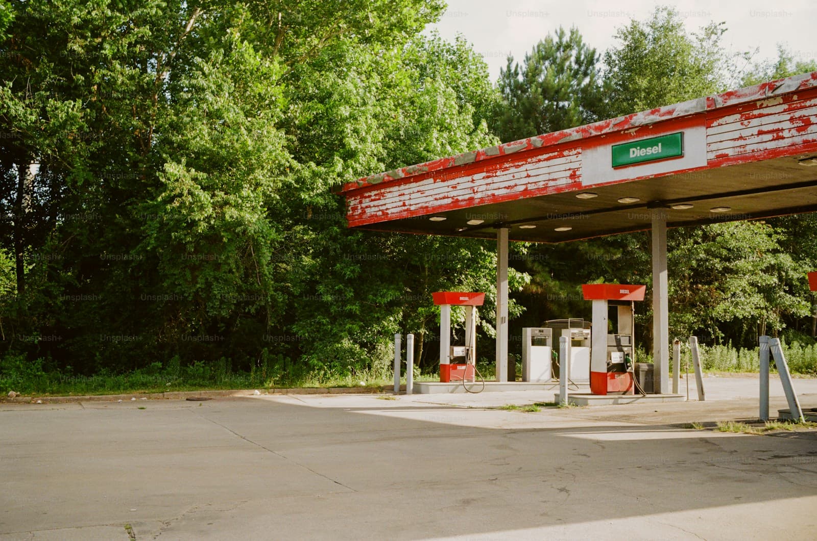 Gas station with red and white striped canopy and fuel pumps surrounded by green trees