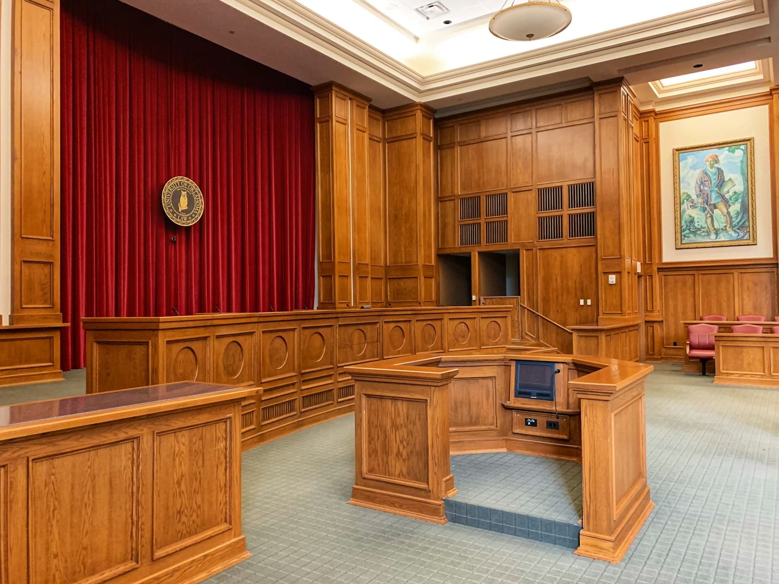 Formal courtroom with wood paneling, red curtains, judge's bench and jury seating