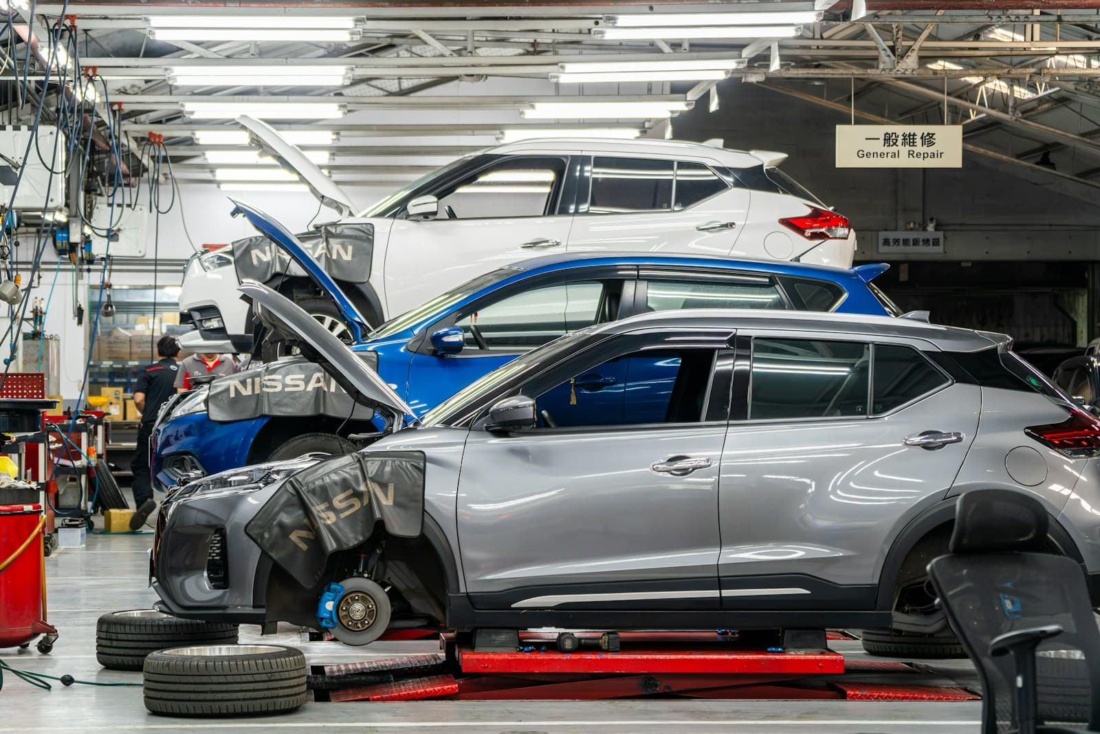 Several cars with hoods raised in a repair garage bay surrounded by tools and tires