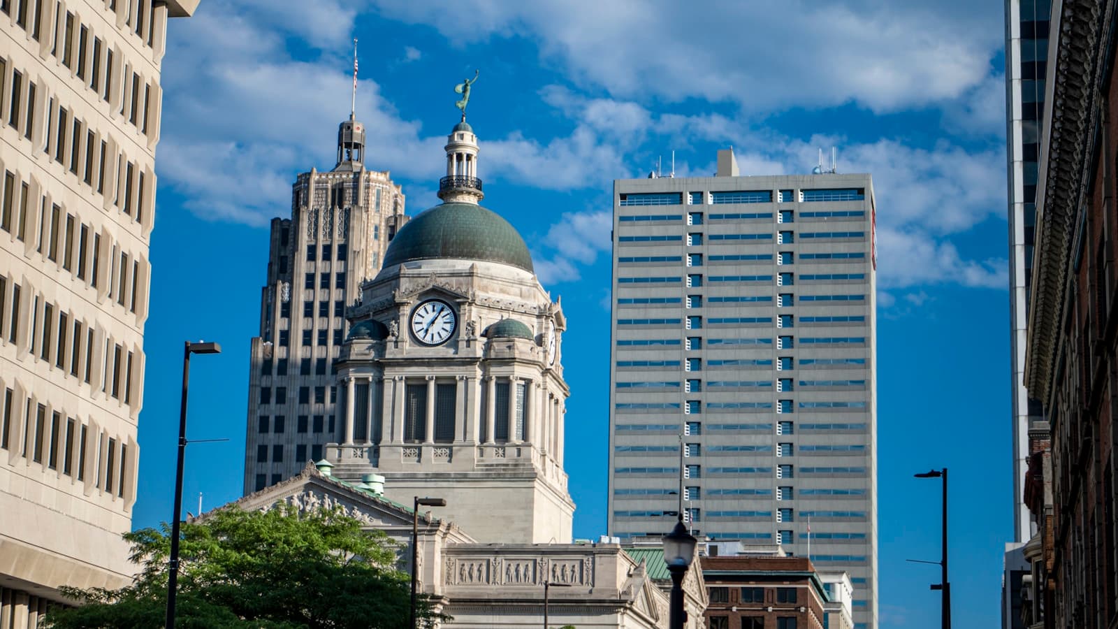 Historic domed government building with clock tower surrounded by modern office buildings in downtown cityscape