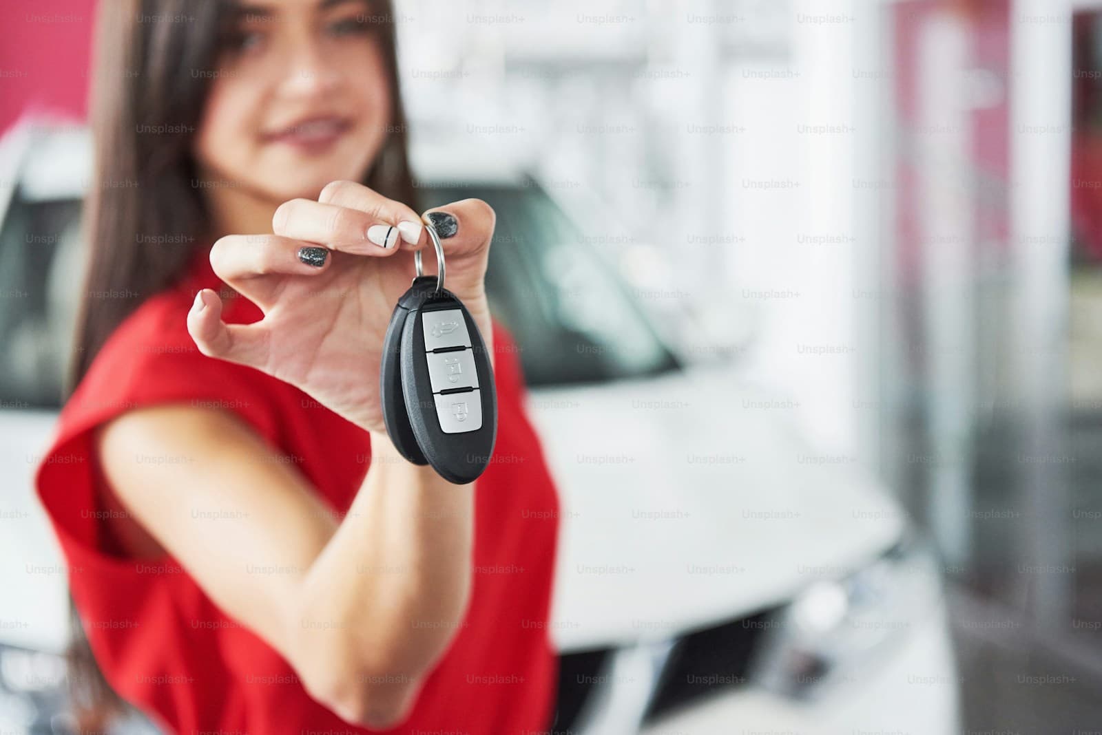 Woman in red shirt holding out car keys at automotive dealership with cars in background