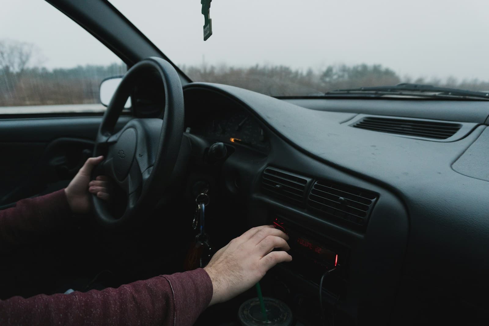 Driver in a burgundy sweater reaching toward the center console on an overcast day
