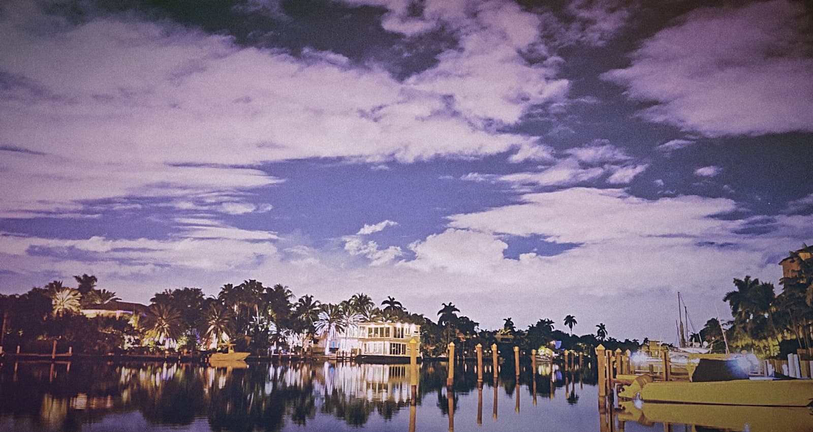 Waterfront homes with boats and docks reflected in calm water under a dramatic purple twilight sky