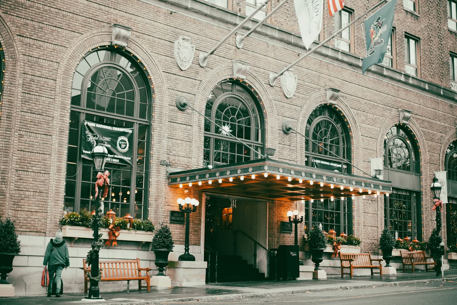 Brick building with arched green windows and lit entrance canopy, outdoor seating visible