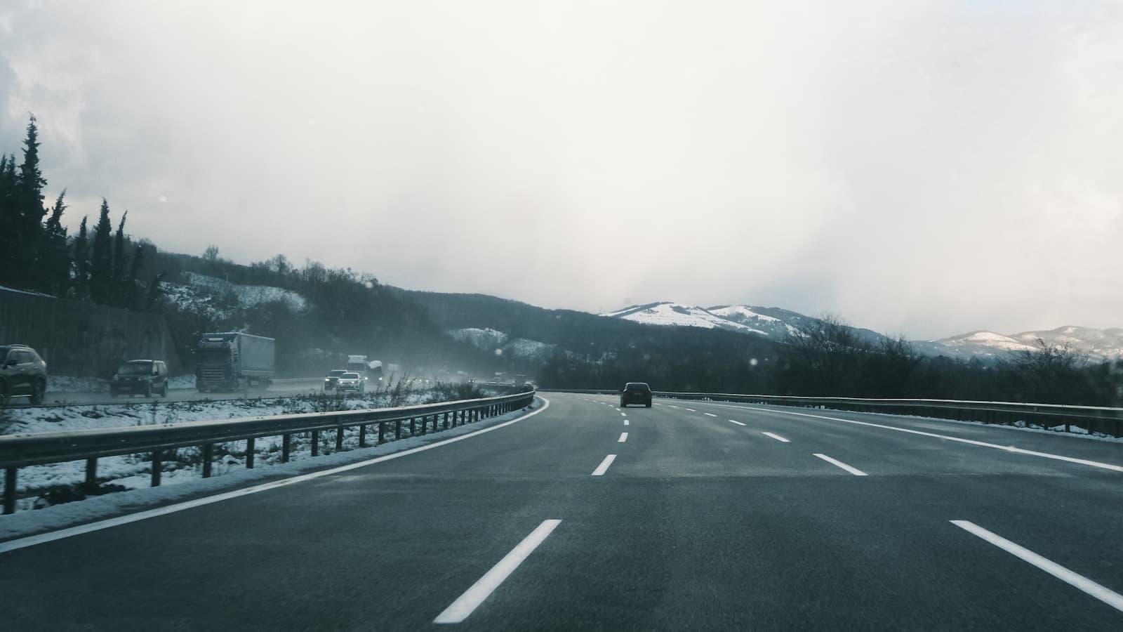 Car on a curved highway through a snowy mountain landscape of evergreens and distant peaks