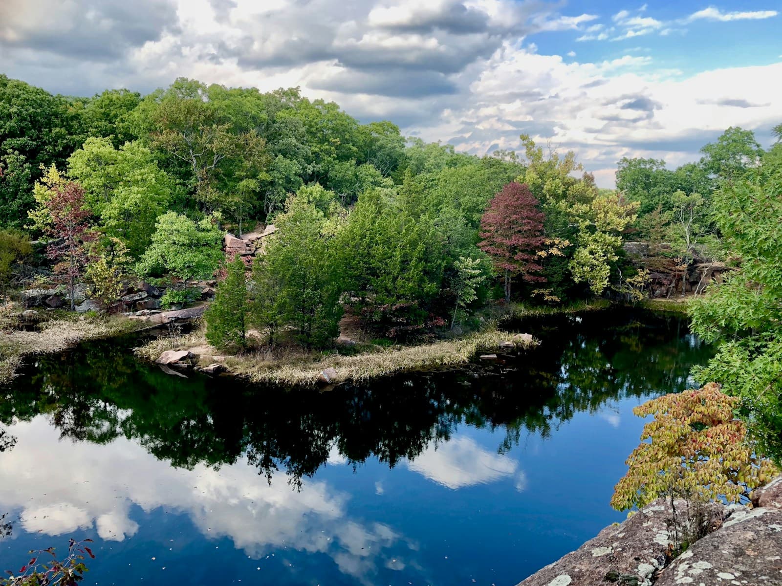 Tranquil lake reflecting clouds and sky, surrounded by green trees and colorful spring foliage
