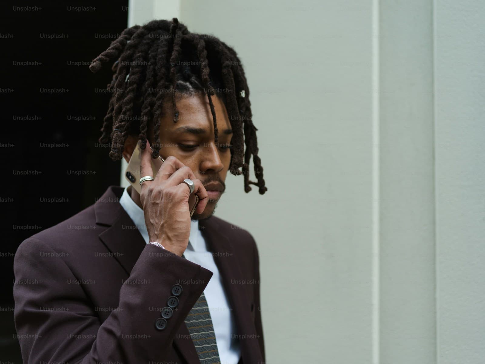 Person with dreadlocks in dark suit talking on mobile phone against white background
