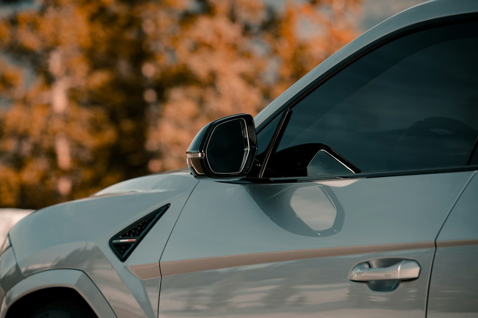 Close side view of a white luxury car parked against warm autumn foliage