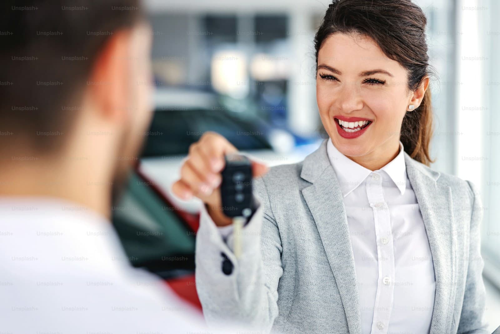 Smiling businesswoman in gray suit handing car keys to customer at auto dealership