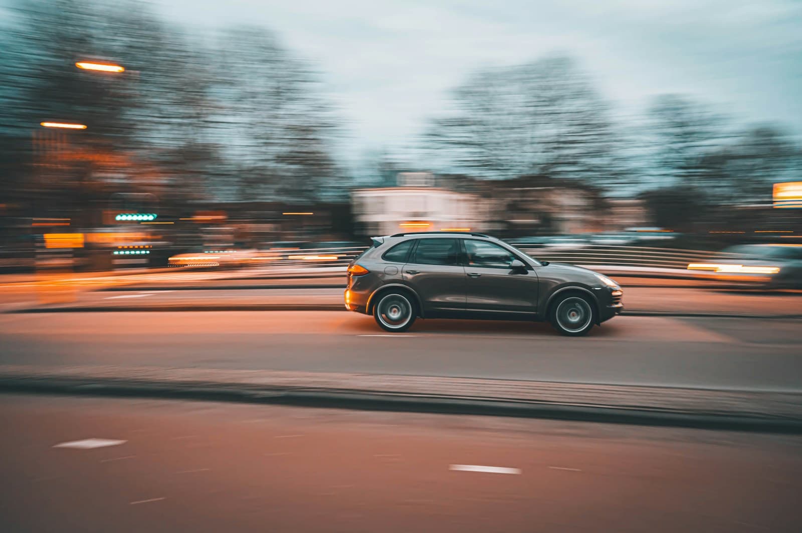 Dark SUV in motion blur driving through city street at dusk with streaked lights and blurred urban background