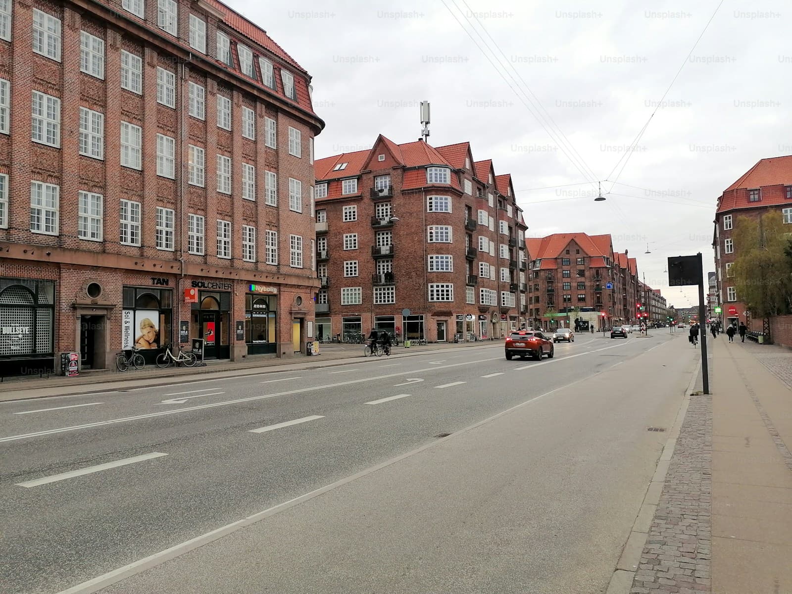 European city street with traditional brick buildings, red tile roofs, and wide roadway on overcast day