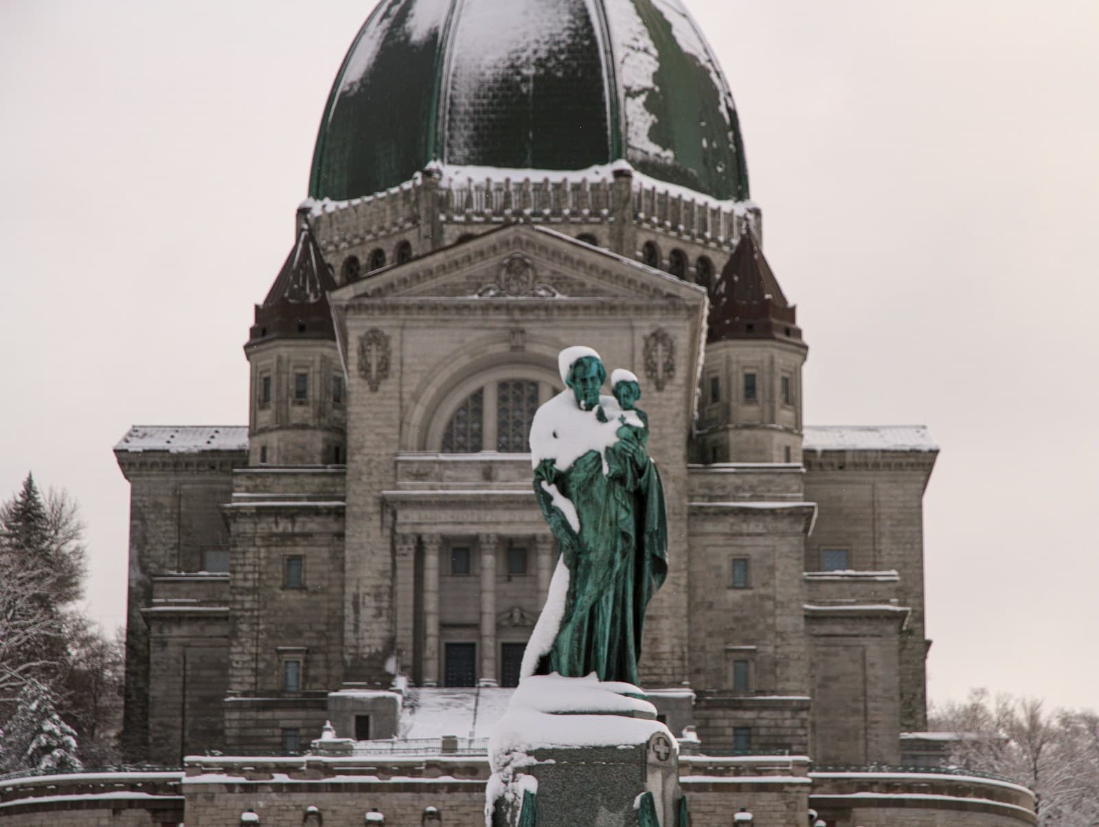Snow-covered bronze statue in front of a historic domed building with green copper dome in winter