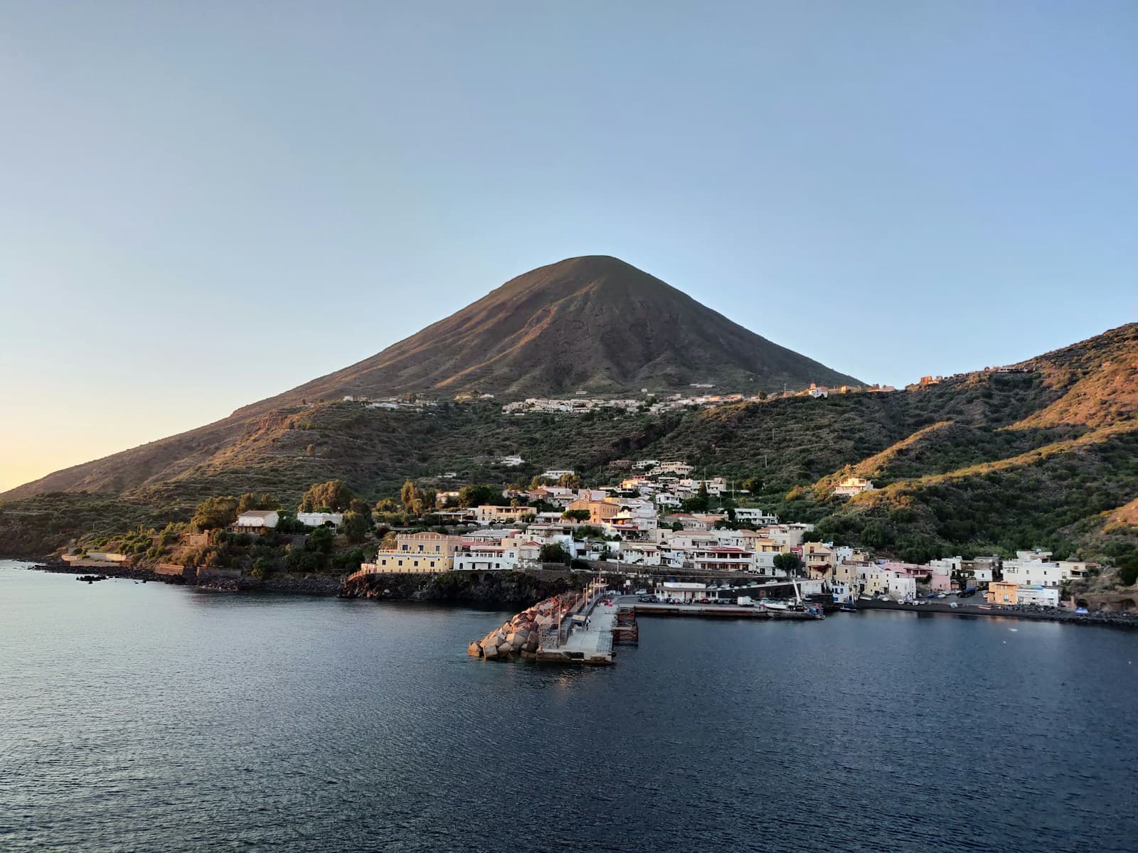 Coastal village with white buildings in a bay beneath a volcanic mountain at sunset