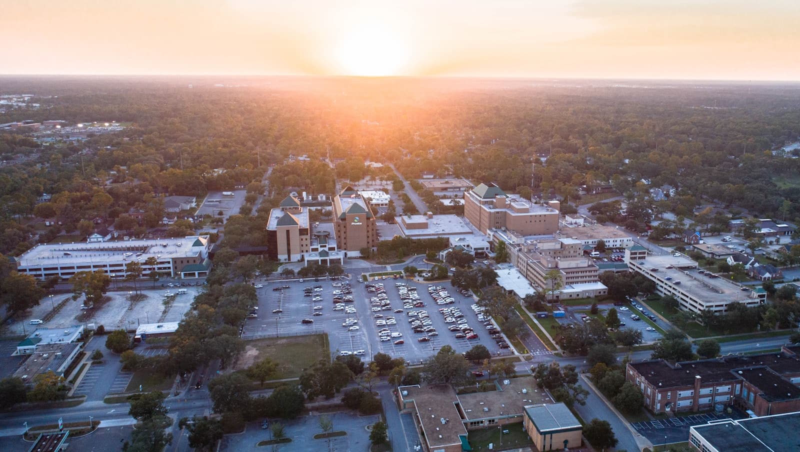 Aerial view of suburban town at sunset with buildings, parking lots, and tree-lined streets in golden light