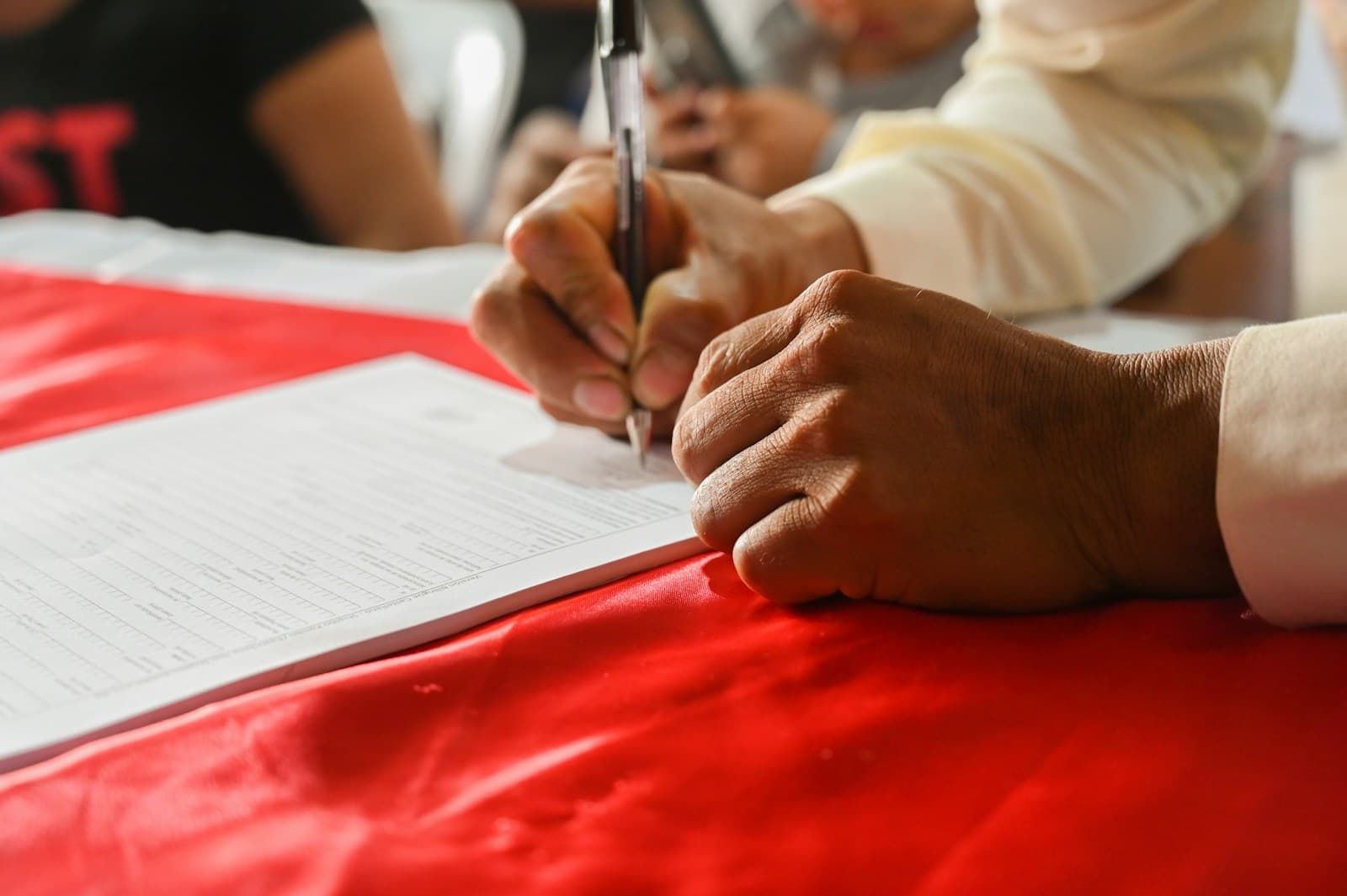 Hands writing on white documents laid across a red surface