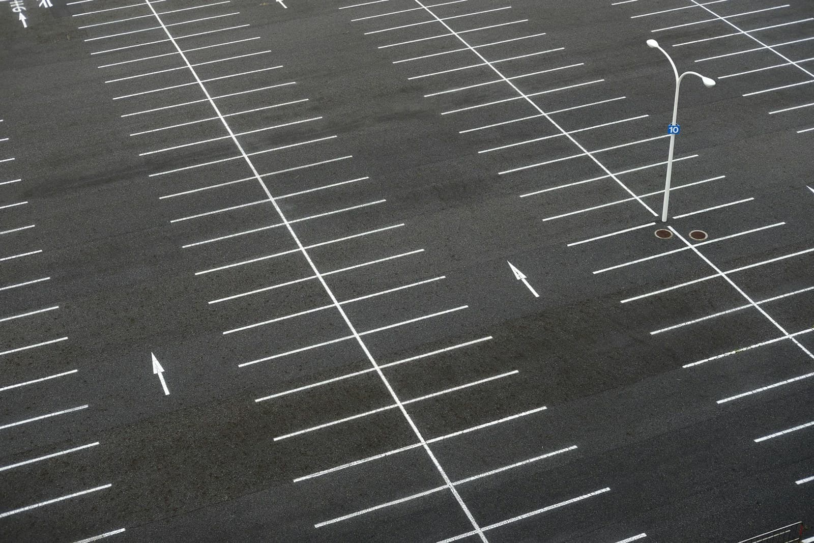 Aerial view of empty parking lot with white painted lines marking parking spaces on dark asphalt