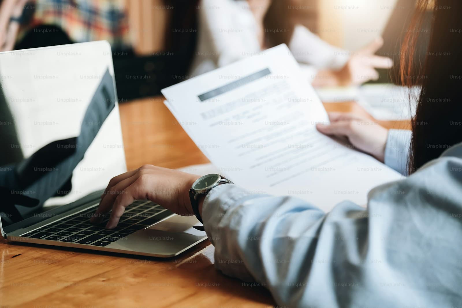 Person typing on laptop with business documents and papers on wooden desk