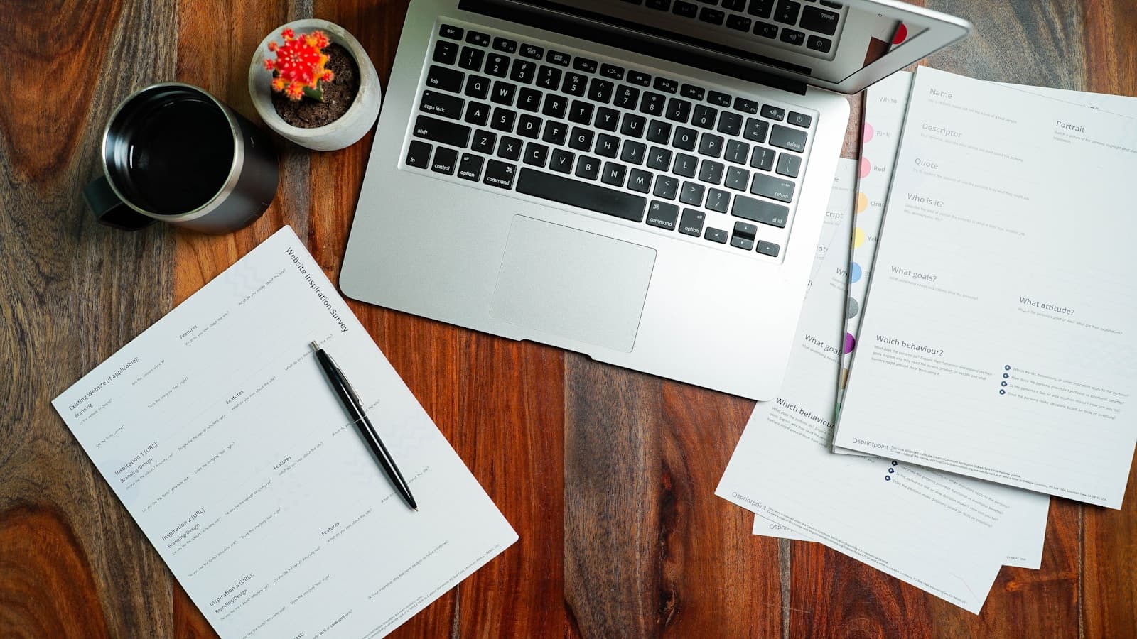 Overhead view of laptop, papers, coffee mug and small plant arranged on wooden desk - home office workspace