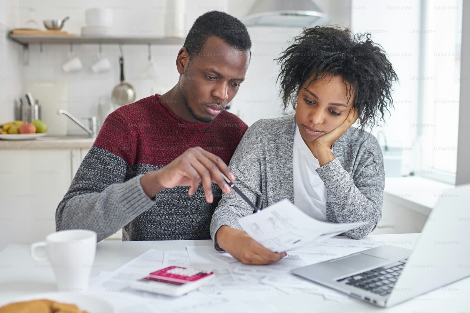 Young couple at a kitchen table reviewing documents together on a laptop