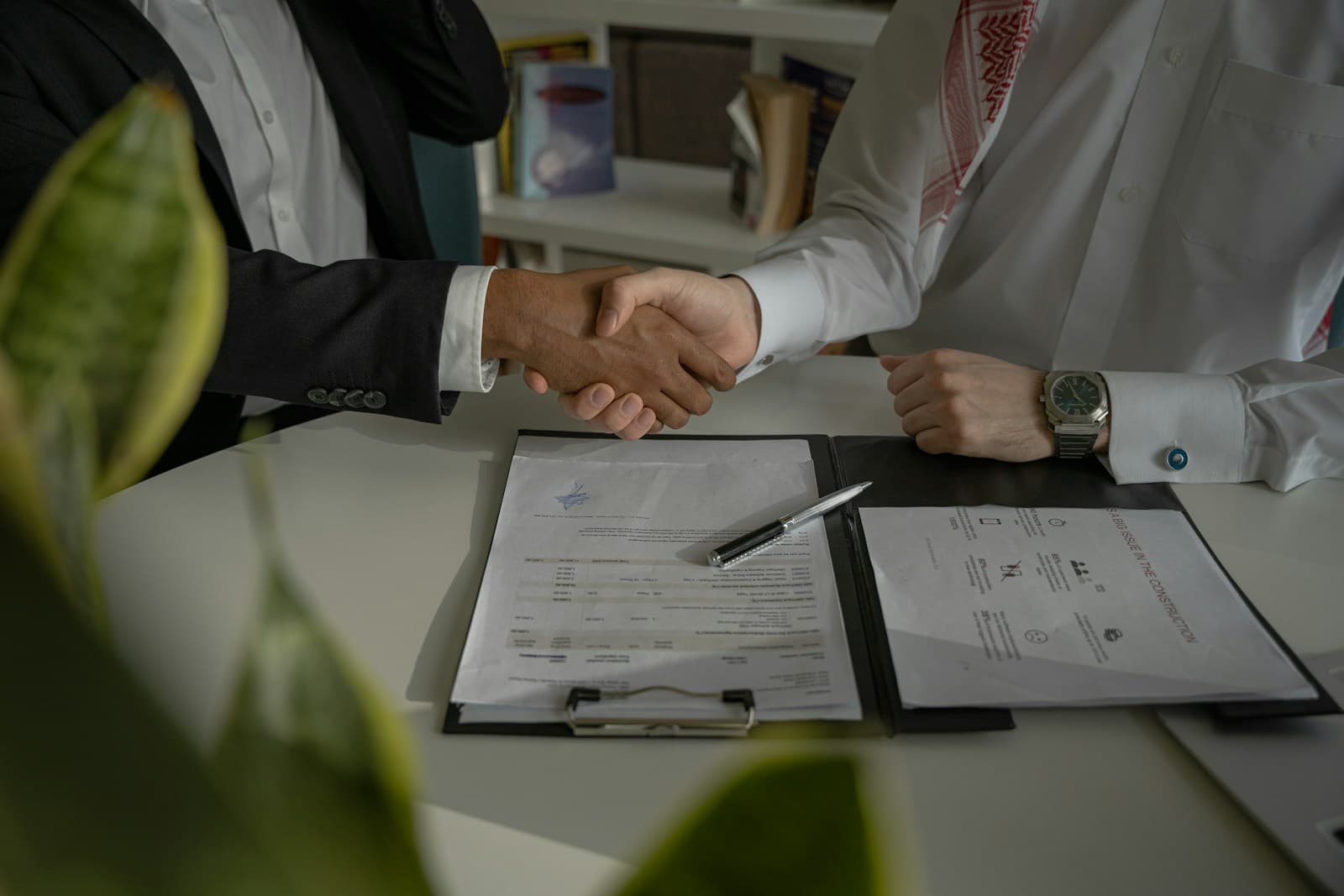 Two men in traditional white dress shaking hands over signed documents