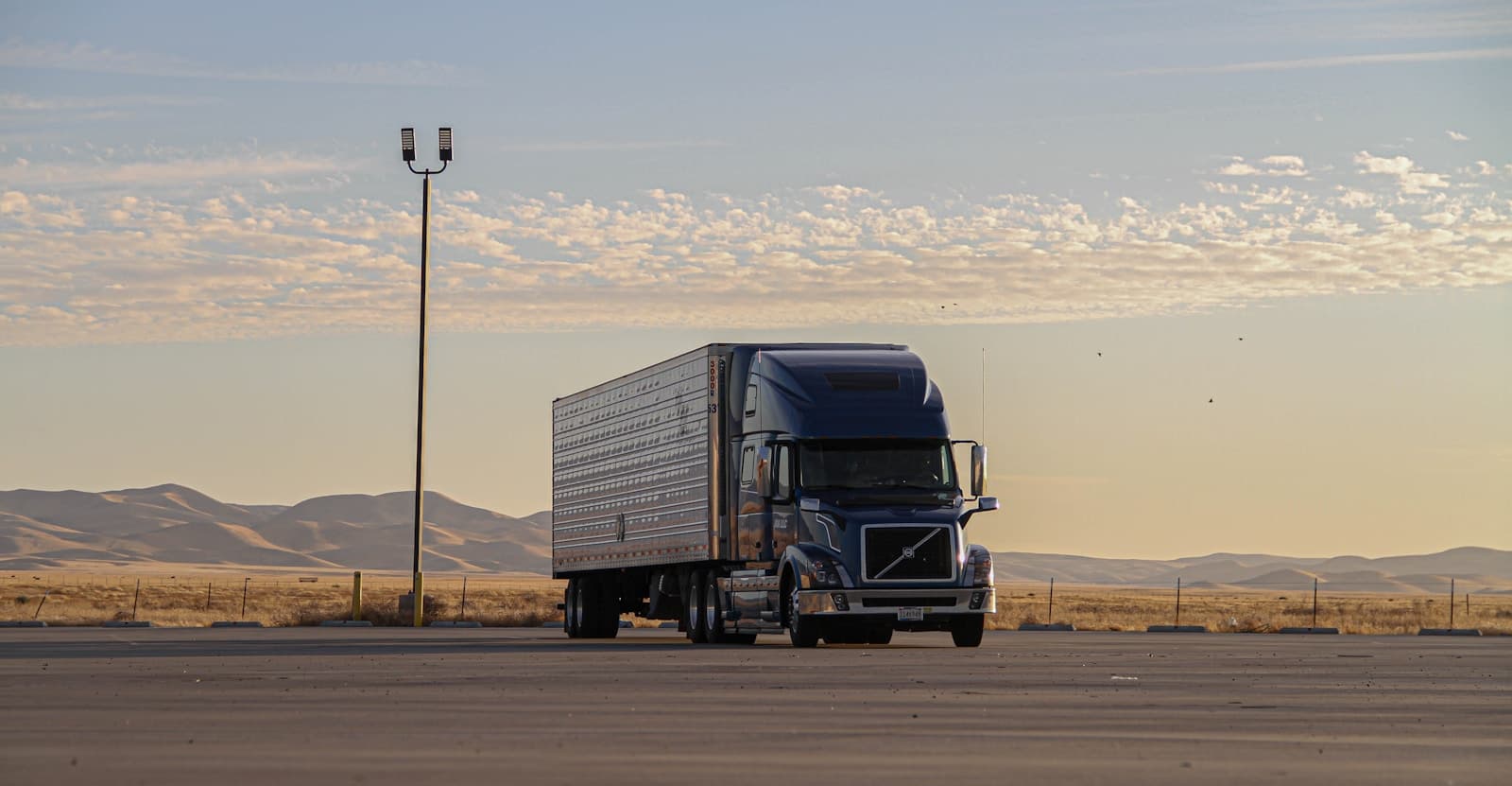 Semi-truck and trailer parked at a desert rest area with mountains at golden hour