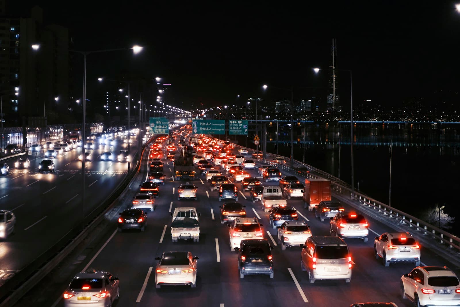 Heavy nighttime traffic with light trails on a multi-lane highway bridge with city lights in background