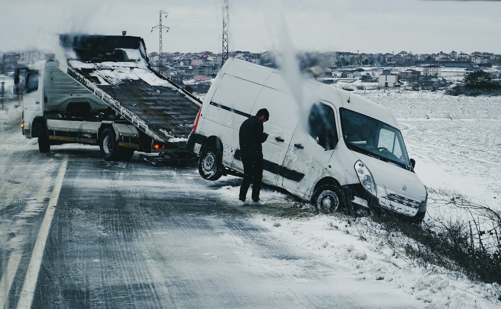White van slid into a snowy ditch as a tow truck prepares to pull it out