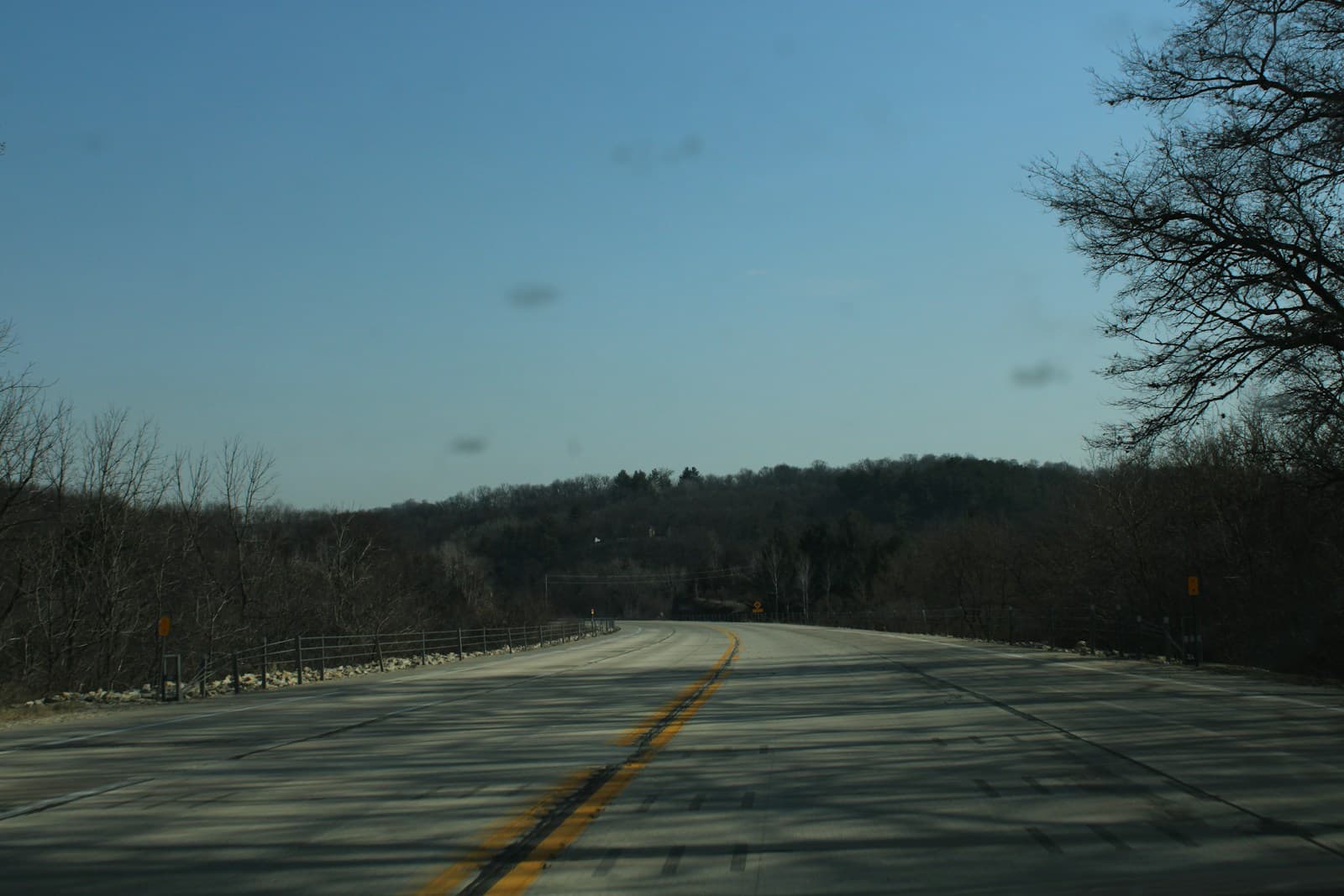Empty rural road with yellow center line stretching toward hills under overcast sky with bare winter trees